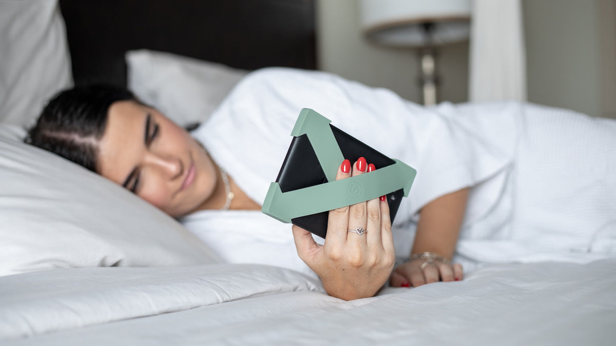 Reading a Kindle in bed with sage green Strapsicle straps holding the device