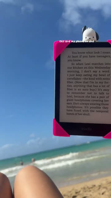 Kindle held up on the beach with pink Strapsicle straps