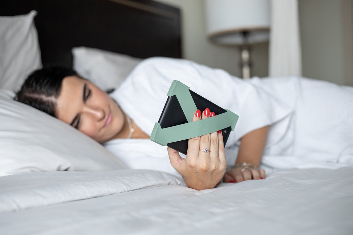 Reading a Kindle in bed with sage green Strapsicle straps holding the device