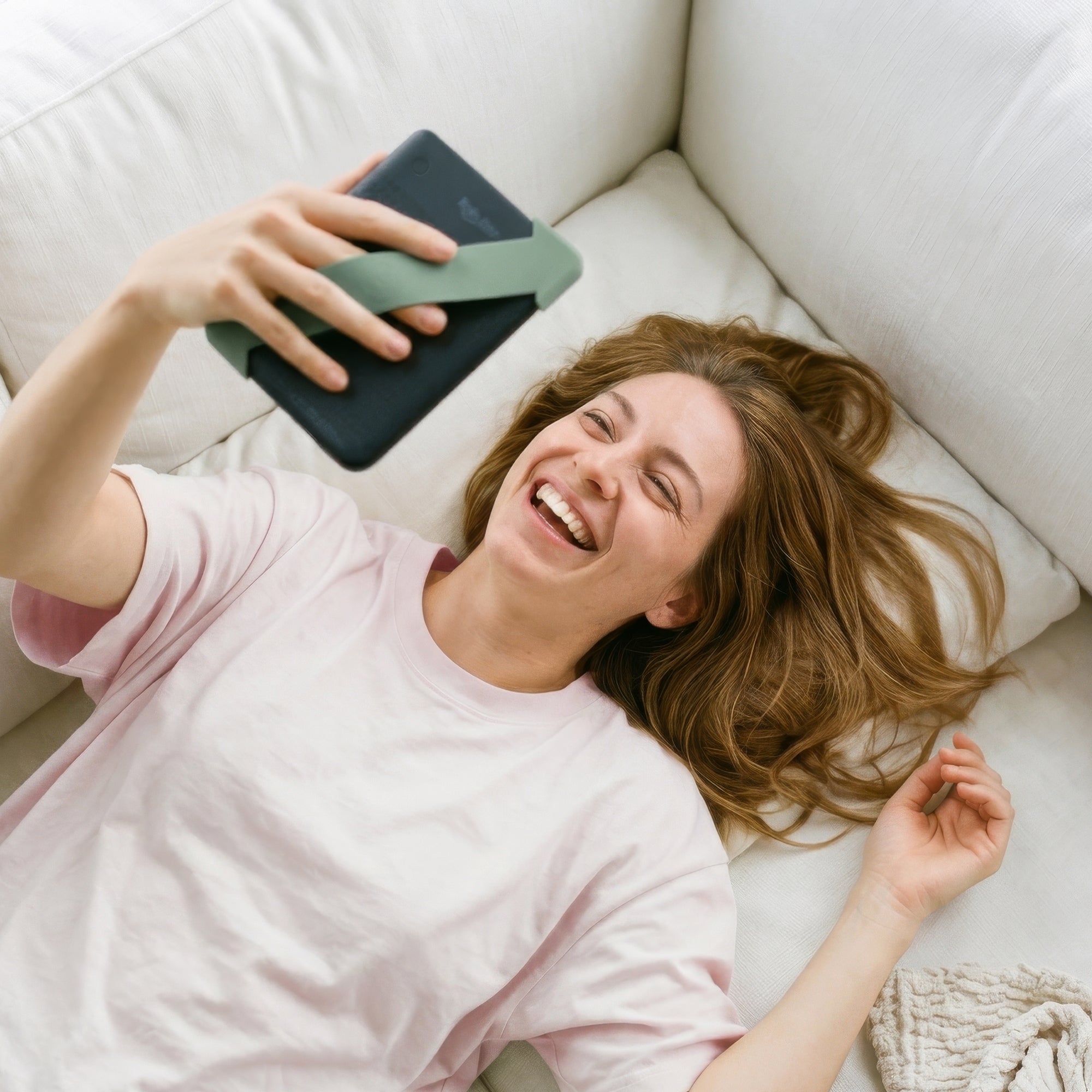 Kindle with sage green Strapsicle straps resting securely on a couch