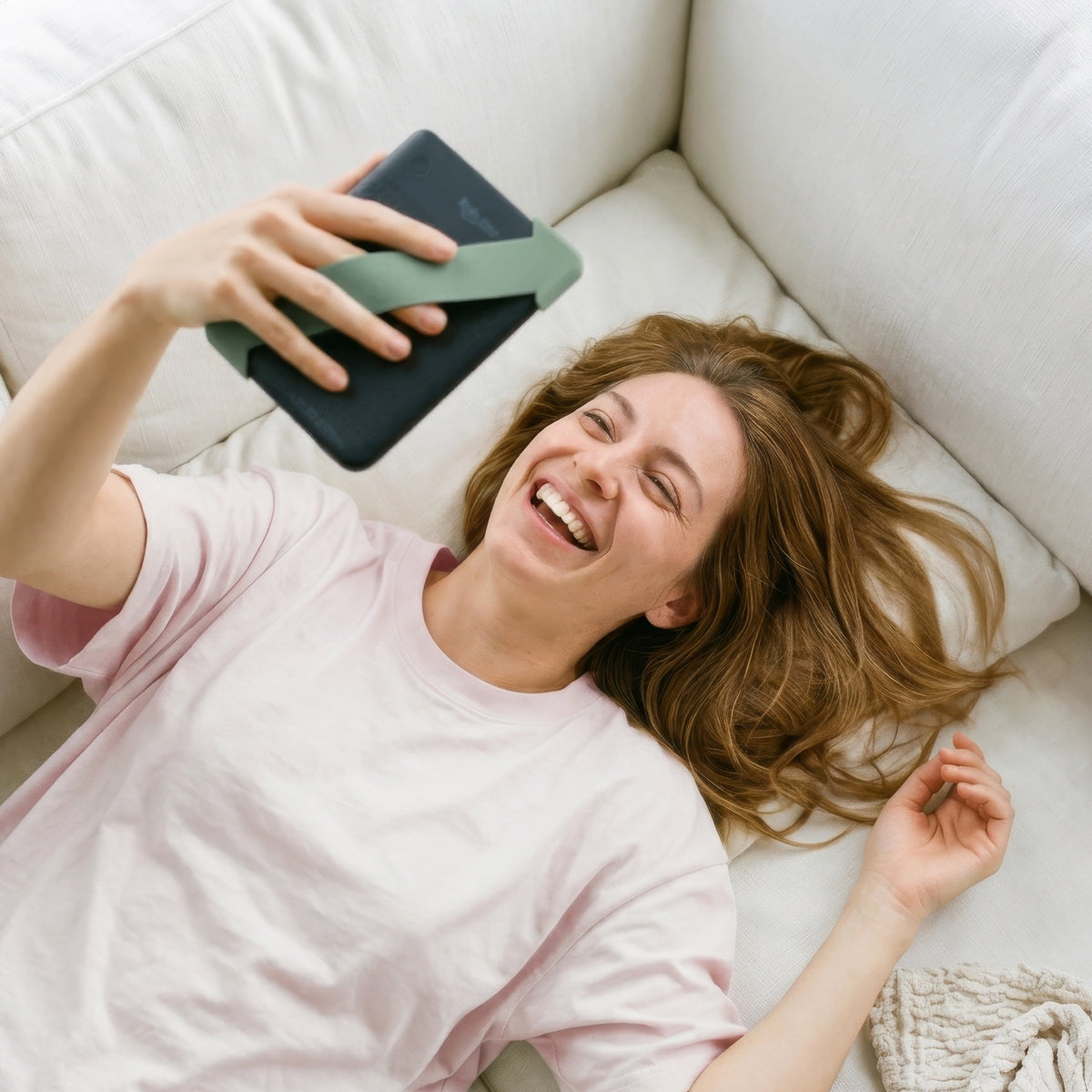 Kindle with sage green Strapsicle straps resting securely on a couch