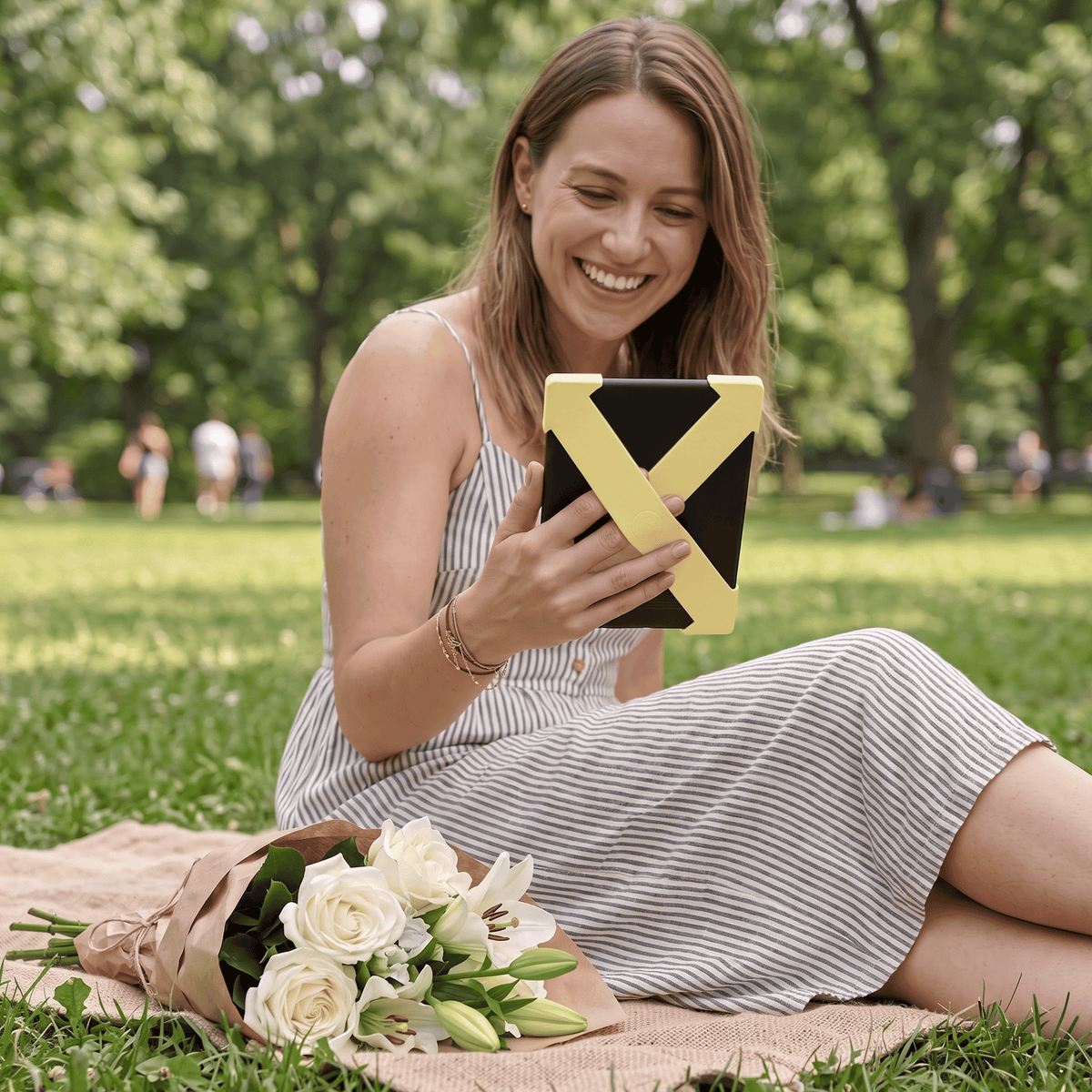 Butter Yellow Strapsicle Straps on a Kindle, held one-handed at a park picnic | Buy Kindle Accessories Direct
